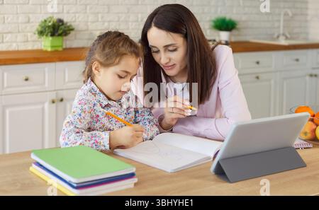 Attività di apprendimento online di madre e figlia utilizzando un tablet, seduti insieme a tavola Foto Stock