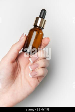 L'estetista tiene in mano il flacone contagocce in vetro ambrato con elementi dorati su sfondo bianco e spazio di copia Foto Stock