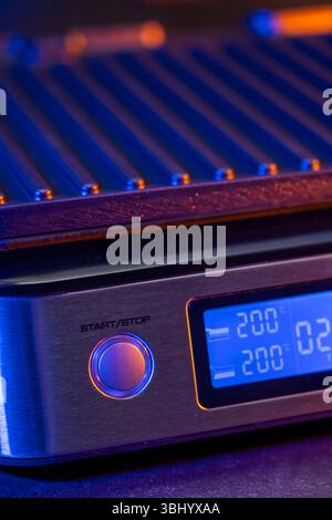 Griglia elettrica con display digitale che mostra temperatura e timer, illuminata da luce blu e arancione Foto Stock
