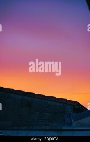 Cielo multicolore in una mattinata all'alba in Francia sulla cima di una parete di mattoni grigi e tegole Foto Stock