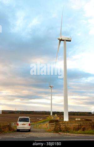 grandi turbine eoliche alte in un vasto paesaggio rurale del northumberland con un cielo nuvoloso nel regno unito e camper nelle vicinanze che mostra dimensioni Foto Stock