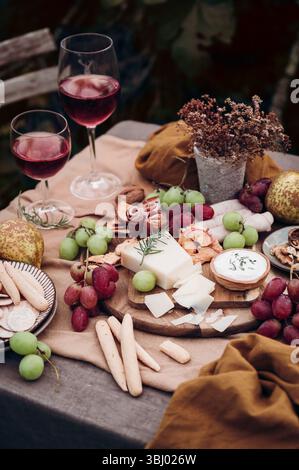 Un ambiente elegante con un tagliere di formaggi, uva assortita, grissini e affettati. Due bicchieri di vino rosso completano la disposizione degli spuntini gourmet, Foto Stock