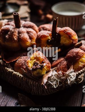 Un cestino accogliente pieno di ciambelle fatte in casa a forma di zucca, guarnite con zucchero e un tocco di cannella. L'ambiente caldo e invitante è perfetto per Foto Stock