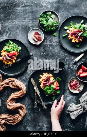 Elegante piatto gourmet con waffle di zucca splendidamente conditi con prosciutto iberico salato, verdure fresche e fette di pomodoro maturo, per creare un delizioso piatto Foto Stock