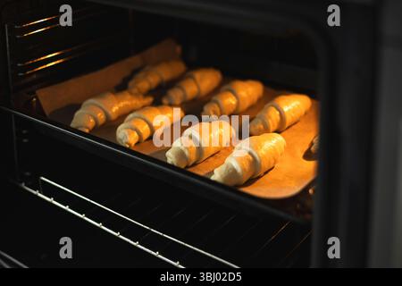Croissant appena sfornati su carta pergamena in forno. I dolci dorati sono perfettamente allineati, catturando il calore e l'aroma di un coz Foto Stock