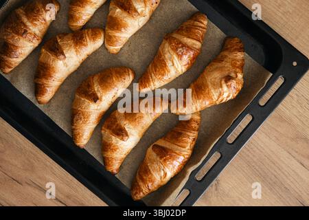 Deliziosi croissant fatti in casa appena sfornati alla perfezione dorata, rinfrescati su un vassoio da forno rivestito in pergamena, catturando il calore e il fascino della cottura casalinga Foto Stock