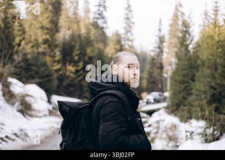 Un giovane vestito con abiti caldi cammina attraverso un sentiero boschivo innevato. Incarna l'avventura e l'esplorazione, godendosi la serena bellezza di nat Foto Stock
