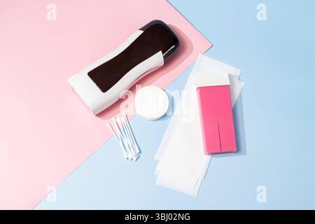 Kit di ceretta roll-on su sfondo rosa pastello e blu, comprensivo di riscaldatore per paraffina, cartucce, tamponi di cotone e bastoncini, perfetto per il gro personale Foto Stock