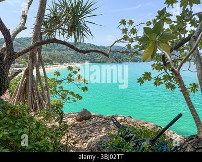 Splendida vista costiera a Phuket, Thailandia, con acque turchesi incorniciate da lussureggianti alberi verdi. Il tranquillo paesaggio mette in risalto la natura dell'isola Foto Stock