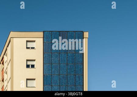 Moderno edificio di appartamenti con pannelli solari sulle pareti esterne sotto il cielo blu. Concetto di ecologia urbana, energia rinnovabile, sostenibilità e città verde Foto Stock