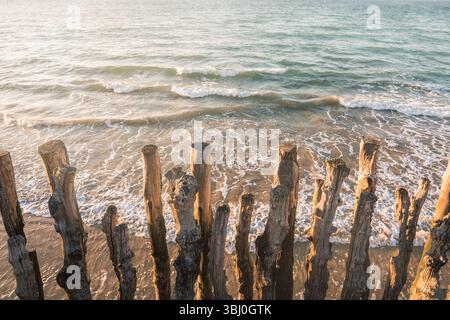 Frangiflutti in legno sulla spiaggia di Saint-Malo, catturati con delicati toni pastello. Onde delicate e luce calda creano un'atmosfera tranquilla e artistica Foto Stock