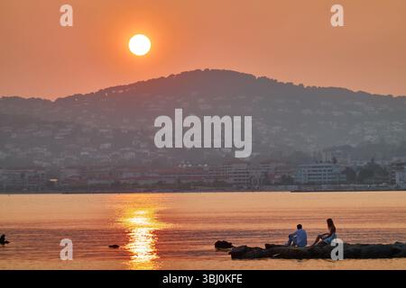 Tramonto sereno sulle colline con una giovane coppia sulle rocce che si rilassa sul mare calmo Foto Stock