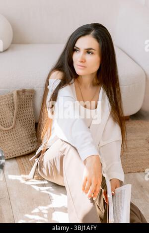 Ritratto di una donna elegante con capelli lunghi che reggono un libro in una camera accogliente Foto Stock