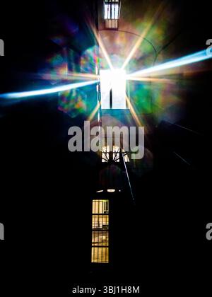 Una luce brillante splende attraverso una finestra, creando un effetto stellare con rifrazioni colorate. L'immagine è presa da un interno scuro, forse un bui Foto Stock