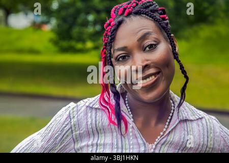 Felice donna afroamericana Ritratto all'aperto trecce colorate sorridenti Foto Stock