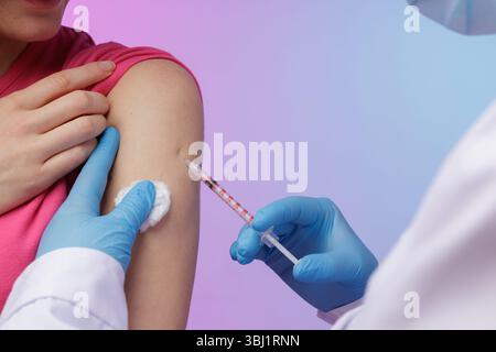 Medico in guanti che somministrano l'iniezione di vaccino al braccio del paziente durante la procedura di immunizzazione, primo piano che mostra siringa, tampone di cotone e azione protettiva. Foto Stock