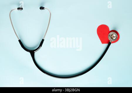 Uno stetoscopio e un cuore rosso di carta simbolica su sfondo azzurro. Vista dall'alto del concetto di salute. Foto Stock