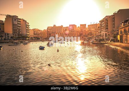 Splendida vista panoramica del tramonto sulla Baia di Spinola a San Giuliano (San Ġiljan), Malta, con molte barche da pesca ancorate nella baia Foto Stock