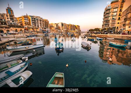 Splendida vista panoramica del tramonto sulla Baia di Spinola a San Giuliano (San Ġiljan), Malta, con molte barche da pesca ancorate nella baia Foto Stock