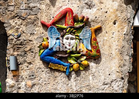 Taormina, Sizilien - Italia - 05-04-2025: Colorata decorazione ceramica della Trinacria con un volto, ali, serpenti e gambe montate su un muro di pietra. Locati Foto Stock
