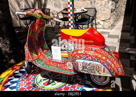 Taormina, Sizilien - Italia - 05-04-2025: Vespa Carretto colorata con motivi e scene tradizionali siciliane è esposta su una base piastrellata accanto a ca Foto Stock