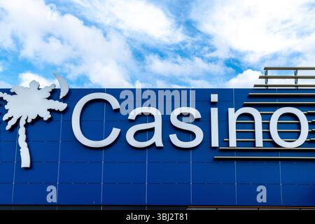 Denia, Alicante - Spagna - 11-26-2024: Un grande cartello bianco del casinò con un logo stilizzato di palma è montato su un moderno edificio blu. Il cielo nella ba Foto Stock