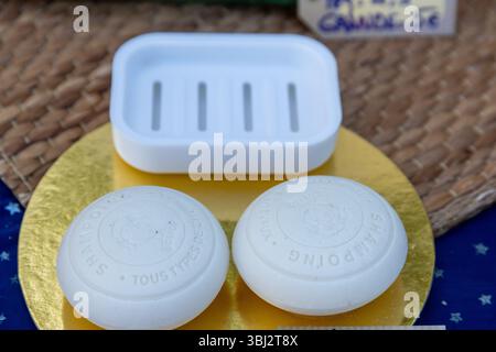 Denia, Alicante - Spagna - 12-01-2024: Due barre di shampoo rotonde con testo in rilievo sono posizionate accanto a un piatto di sapone bianco. Gli oggetti poggiano su un ci dorato Foto Stock