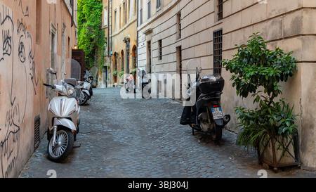 Gli scooter parcheggiavano su una stretta strada acciottolata a Roma, in Italia Foto Stock
