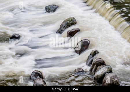 L'acqua del fiume giapponese scorre su lucenti pietre nere Foto Stock