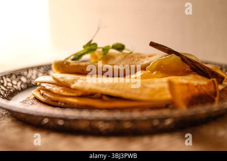 Pila rustica di pancake serviti con fette d'arancia secca e marmellata d'albicocca dorata. Accogliente dessert fatto in casa per colazione, brunch o snack dolci. Foto Stock