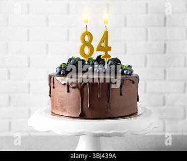 Deliziosa torta al cioccolato con frutti di bosco e candele a forma di numero in fiamme sul tavolo. 84° compleanno o altra occasione speciale Foto Stock