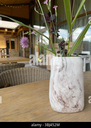 Vaso in marmo con fiori selvatici sul tavolo. Terrazza in estate. Design e mobili in legno. Foto Stock