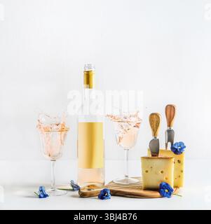 Vino e formaggio con spruzzi di vino e bottiglia di vino con mock-up etichetta vuota, coltelli di formaggio, tagliere e fiori blu. V anteriore Foto Stock