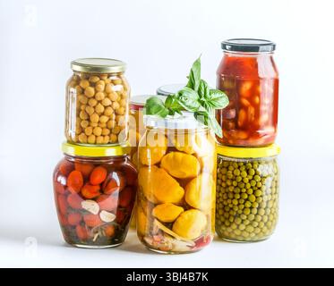 Varie verdure conservate in vasetti di vetro su sfondo bianco. Pomodori in conserva, piselli, ceci, fagioli e zucca. Vista frontale. Foto Stock