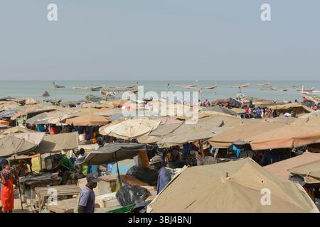 Ombrelloni, bancarelle di cibo all'ombra dal sole presso il frenetico mercato del pesce quotidiano sulla spiaggia di Mbour, Petite Cote, regione di Thies, Senegal, Africa occidentale Foto Stock