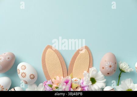 Uova di Pasqua pastello con motivi floreali, orecchie conigliette e fiori primaverili su sfondo blu Foto Stock