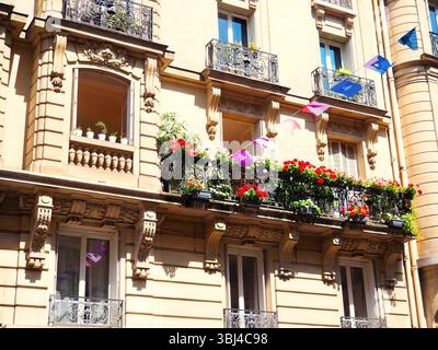 Facciata dell'edificio parigino con balconi pieni di fiori e bandiere festive Foto Stock