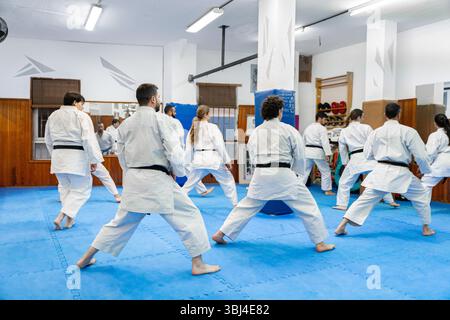 Gruppo di studenti di karate in kimono bianco che praticano arti marziali insieme in un dojo Foto Stock