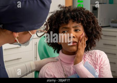Paziente che soffre di mal di denti, discutendo del suo disagio con un dentista in una clinica odontoiatrica durante un esame approfondito Foto Stock