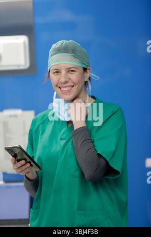 medico donna sorridente alla macchina fotografica con il cellulare in sala operatoria Foto Stock