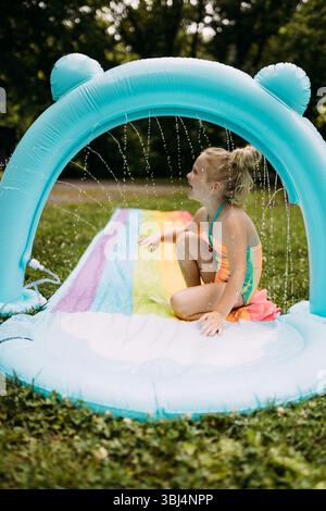 Bambino sorridente che gioca con l'irrigatore arcobaleno nel cortile posteriore Foto Stock