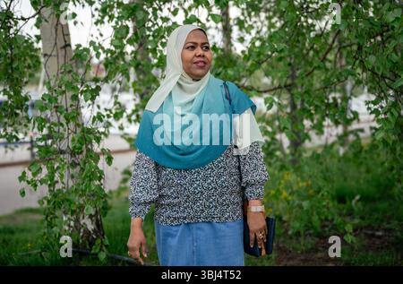 donna in un hijab e camicetta color tè in piedi all'aperto sotto alberi frondosi Foto Stock