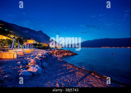 L'alba colorata sul Lago di Garda in Italia, con acque tranquille in primo piano e montagne nebbiose sullo sfondo che creano un ambiente tranquillo e sereno. Foto Stock