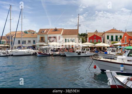 Pittoresco lungomare del villaggio di Fiskardo a Cefalonia, in Grecia, con tradizionali case colorate, barche ormeggiate e una tranquilla vita portuale ionica. Foto Stock