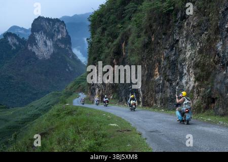 Gruppo di motociclisti che percorrono la strada panoramica tra le montagne carsiche in un giro ad anello di ha Giang nel nord del Vietnam Foto Stock