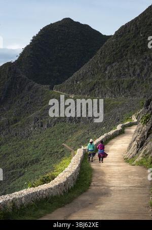 Due donne del posto in abiti tradizionali camminano lungo il passaggio sopraelevato ai margini della montagna Foto Stock