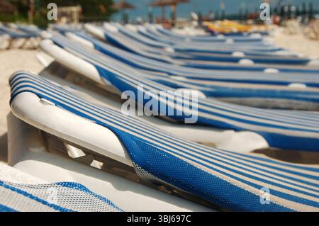 File di lettini da spiaggia a righe blu e bianche allineati su una spiaggia sabbiosa in attesa di prendere il sole Foto Stock