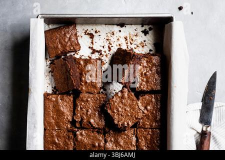 Un vassoio da forno riempito con brownie al cioccolato appena tagliati su carta pergamena. Foto Stock