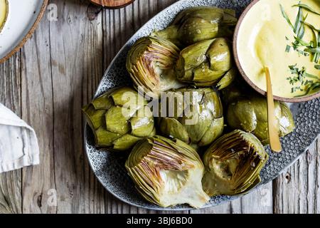 Un piatto di carciofi cotti servito con una salsa cremosa su un rustico tavolo in legno. Foto Stock
