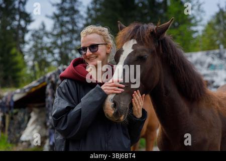 In questa scena emozionante, una giovane donna sorridente interagisce amorevolmente con un cavallo, mostrando il legame tra esseri umani e animali in una natura serena. Foto Stock